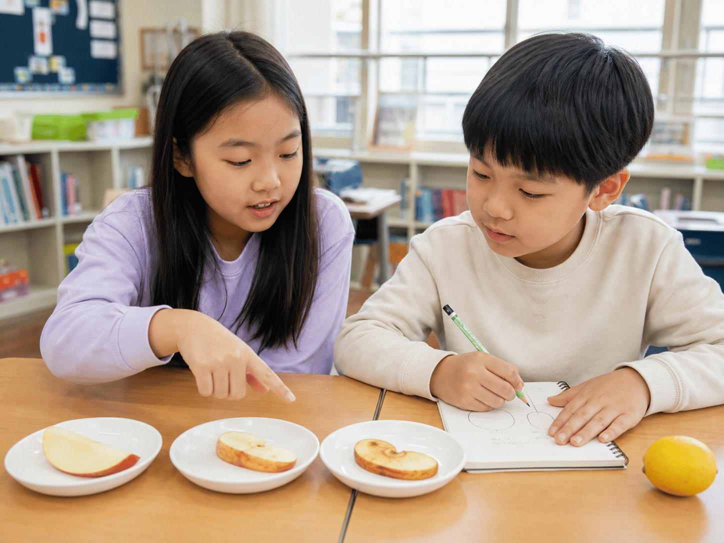 Hai đứa trẻ quan sát ba đĩa táo có mức độ đổi màu khác nhau, ghi chép và thảo luận.